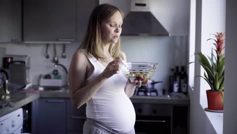 Cheerful-pregnant-woman-eating-salad-and-rubbing-belly